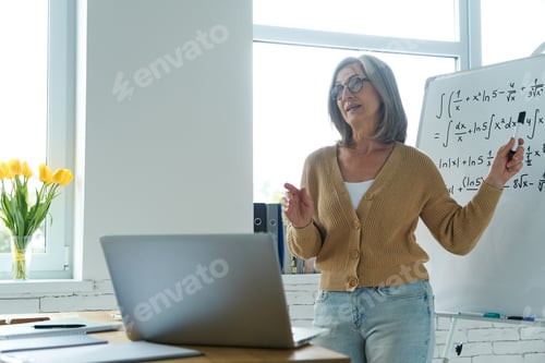 Preview: Confident senior woman pointing whiteboard while standing at the classroom