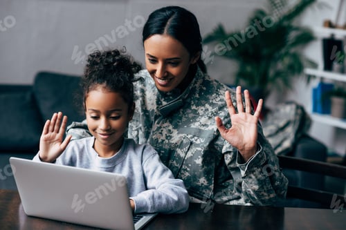 Preview: african american woman in military uniform making video call on laptop with daughter at home