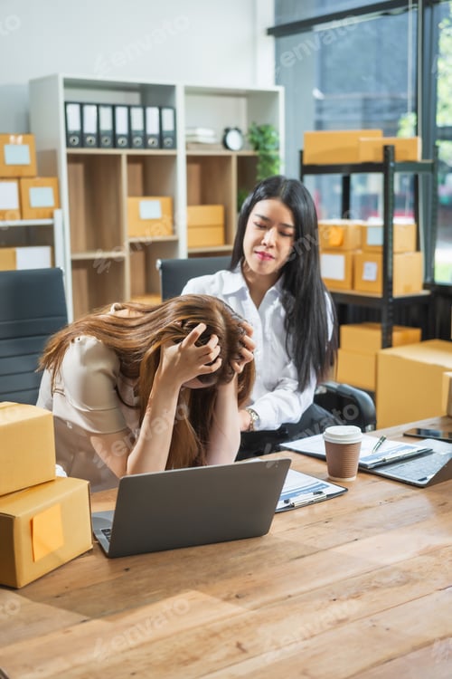 Preview: Two Asian business woman work at their desks, stressed by poor sales not reaching targets.Frequent