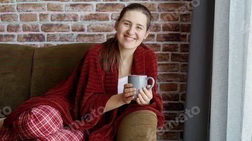 Preview: Happy smiling woman in pajamas resting on sofa with cup of tea. Female resting at home