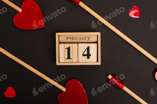 Preview: top view of wooden calendar with 14 february near heart-shaped lollipops on black