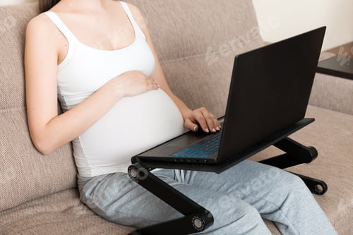 Preview: Pregnant woman using laptop in sofa at home