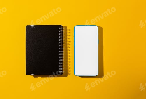 Preview: Top view of a smartphone and a notepad on a yellow background