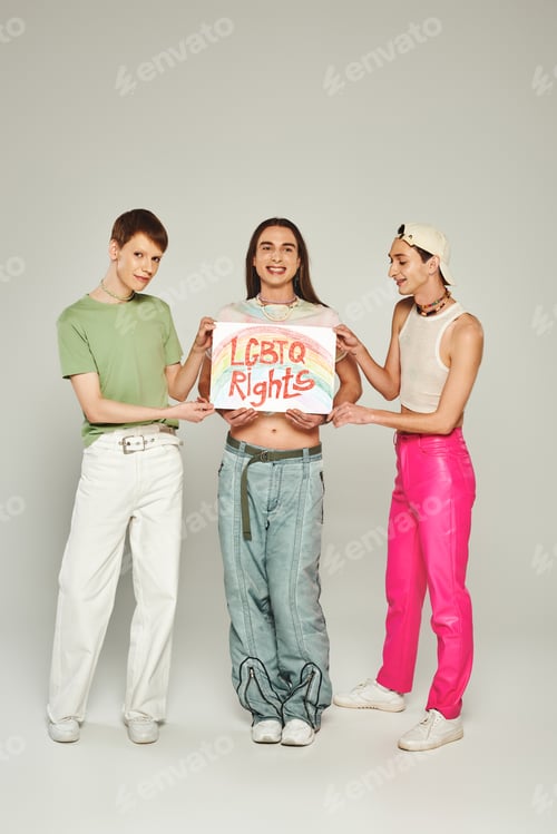 Preview: Smiling and young nonbinary friends holding placard with lgbtq rights lettering and standing