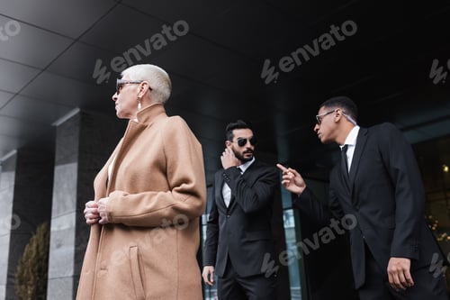 Preview: african american bodyguard pointing with finger near bi-racial colleague and senior business lady
