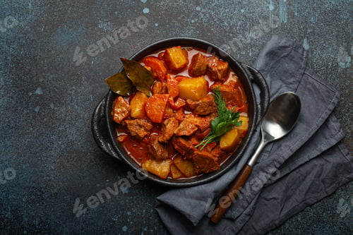 Preview: Beef meat stew with potatoes, carrot and delicious gravy in black casserole pot with bay leaves