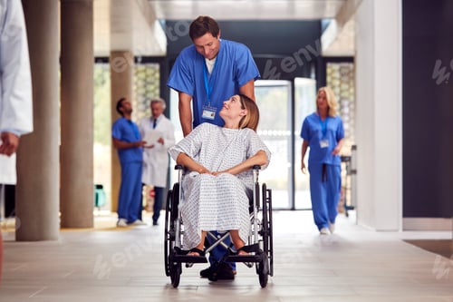Preview: Male Nurse Wearing Scrubs Pushing Female Patient In Wheelchair Through Hospital Building