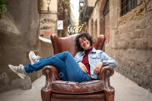 Preview: Smiling tourist relaxing on vintage armchair in Barcelona alleyway