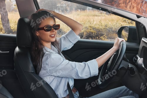 Preview: A woman in sunglasses sits in the driver's seat, her hand on the steering wheel, and her head tilted