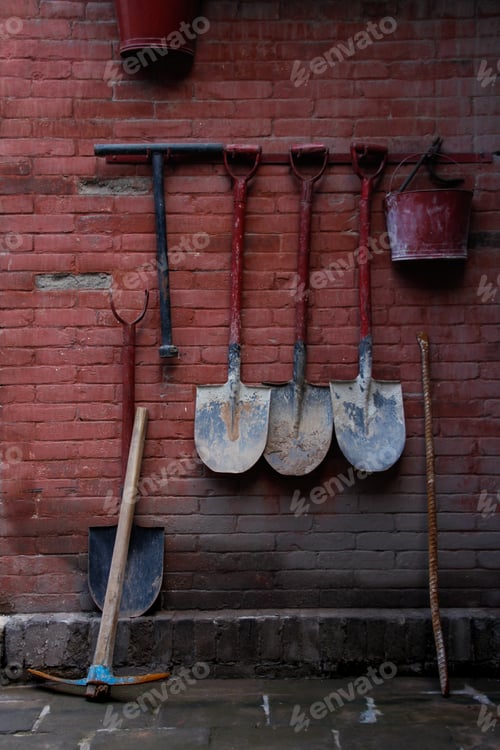 Preview: Set of tools (shovel, pick and bucket) hanging on a red brick wall