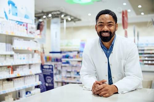 Preview: Friendly Pharmacist Standing in a Modern Pharmacy with Shelves of Medicines