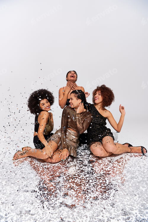 Preview: stylish attractive african american women partying under confetti rain sitting on floor, fashion