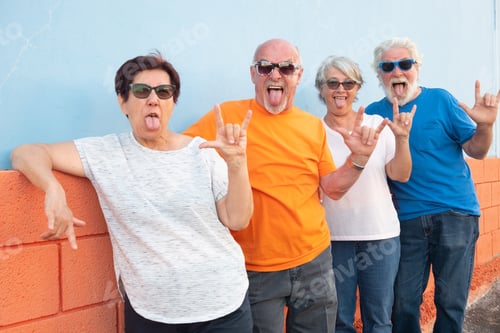 Preview: Group of four senior people have fun standing against an orange and blue wall smiling and gesturing