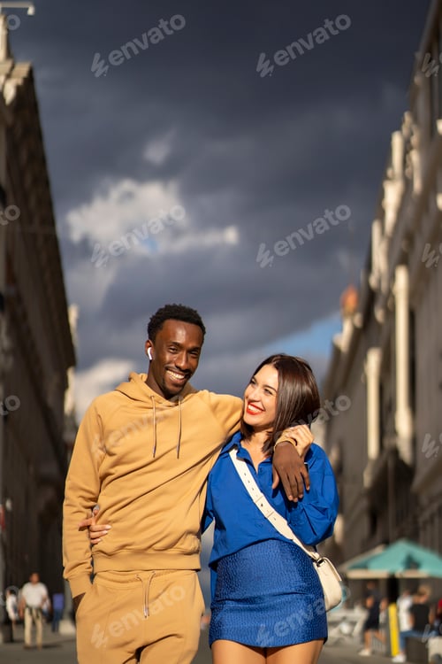 Preview: Romantic couple walking together in stylish outfits under dramatic sky in downtown cityscape