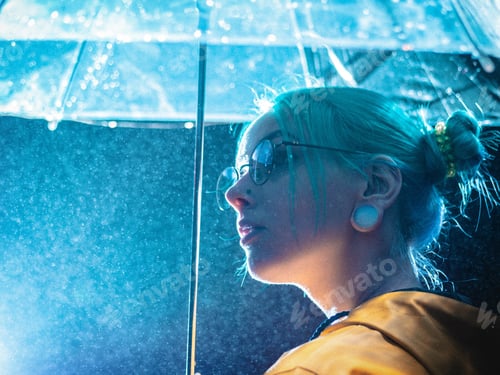 Visualização: Jovem menina bonita com cabelo tingido de azul em capa de chuva amarela e com suportes de guarda-chuva transparentes