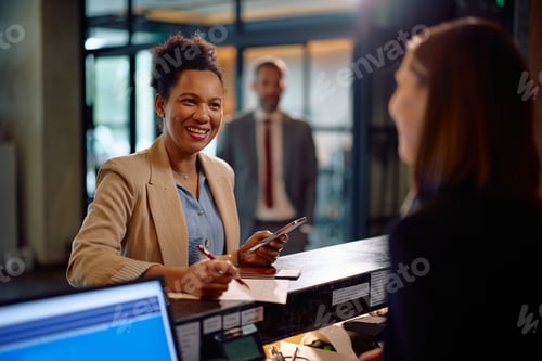 Preview: Happy black woman checking in at hotel reception during her business trip.