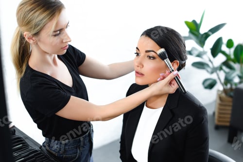 Preview: young businesswoman getting makeup done by makeup artist