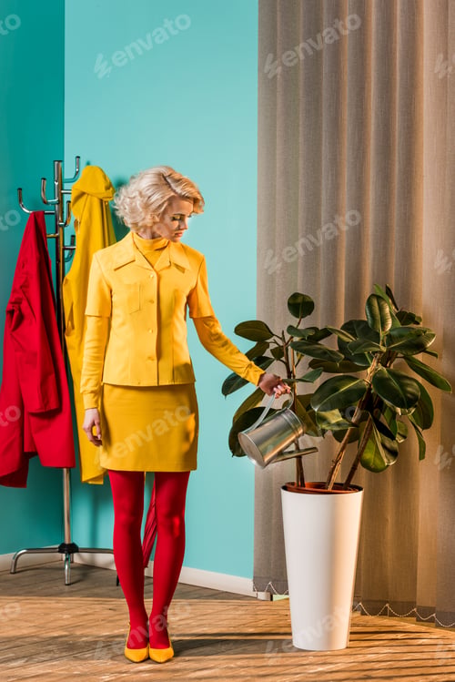 Preview: retro styled beautiful woman in colorful dress watering plant with watering can at home