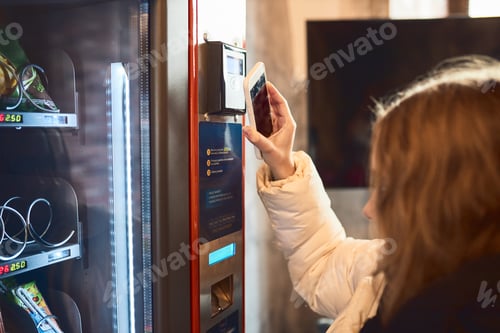 Preview: Woman paying for product at vending machine using contactless method of payment with mobile phone