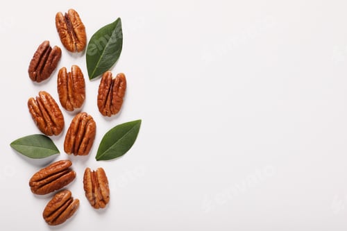 Preview: Delicious pecan nuts and green leaves on white background, flat lay. Space for text