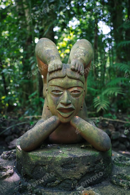 Preview: Vertical closeup of an old Hindi statue covered in leaves and moss in the Jungle