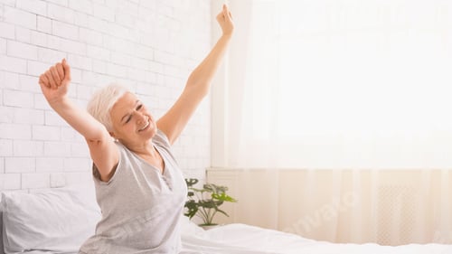 Preview: Joyful Senior Woman Stretching Arms After Waking Up in Bedroom
