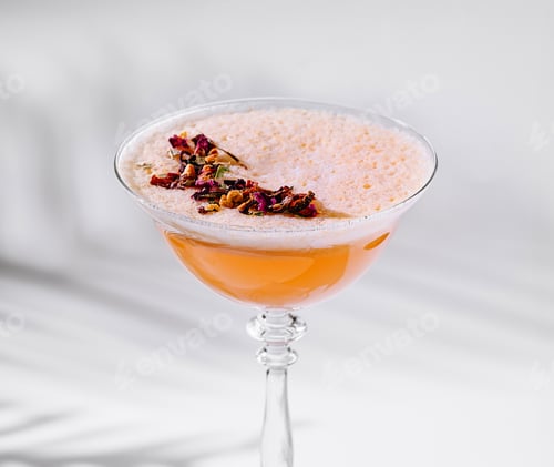 El cóctel de naranja con flores comestibles está de pie sobre una mesa blanca