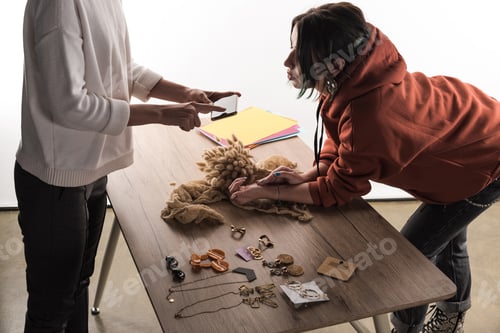 Preview: two commercial photographers taking pictures of composition with flora and accessories on smartphone
