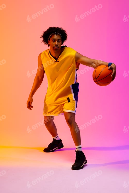 Preview: Image of biracial basketball player bouncing basketball on pink to orange background