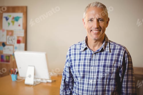 Preview: Man standing next to desk in home office, viewing computer monitor and bulletin board, copy space