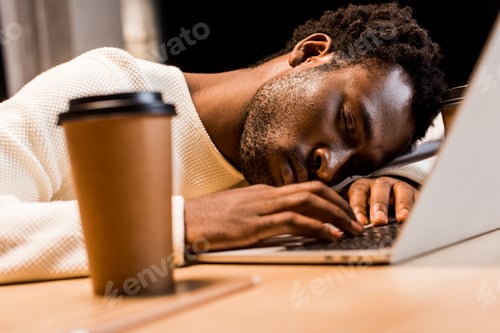 Preview: selective focus of exhausted african american businessman sleeping at workplace near laptop and