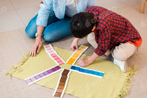 Preview: High angle view of teacher and child playing colorful game on floor in montessori school
