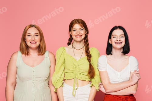 Preview: Cheerful body positive women looking at camera on pink background