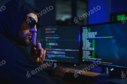 Preview: hacker sitting at desk in dark atmosphere. A computer programmer or hacker.