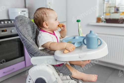 Preview: Baby eating independently in kitchen setting. Complementary feeding