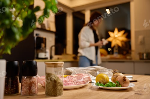 Preview: Fresh ingredients on kitchen table with woman cooking in background