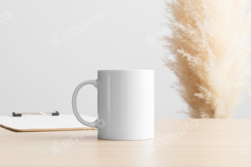 Preview: White mug mockup with a clipboard on the wooden table with a pampas decoration.