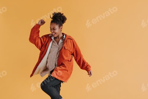 Preview: Joyful african american woman in windbreaker dancing on yellow background. Studio shot of happy bla