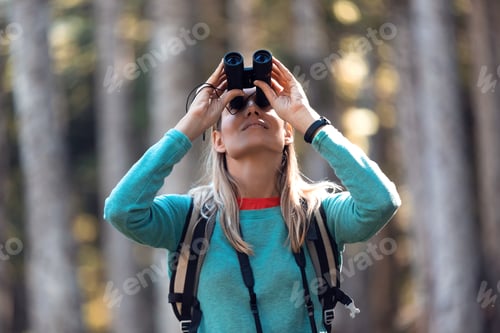 Preview: Hiker young woman looking birds through binoculars telescope in forest.