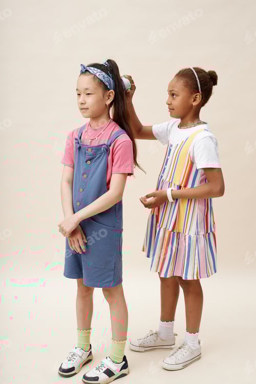Preview: Careful Black Girl in Dress Brushing Hair of Asian Female Friend in Studio