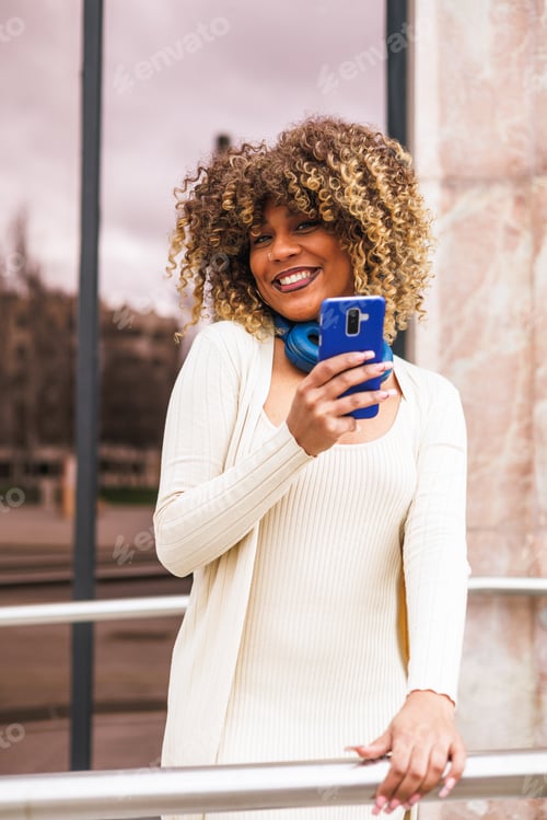 Preview: portrait of modern afro latin woman using smartphone outdoors