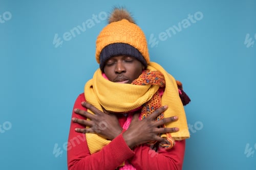 Preview: Funny african american man in yellow scarf and hat freezing in warm clothing.