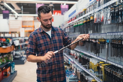 Preview: a buyer in a construction hypermarket chooses a drill for a drill or a screwdriver.
