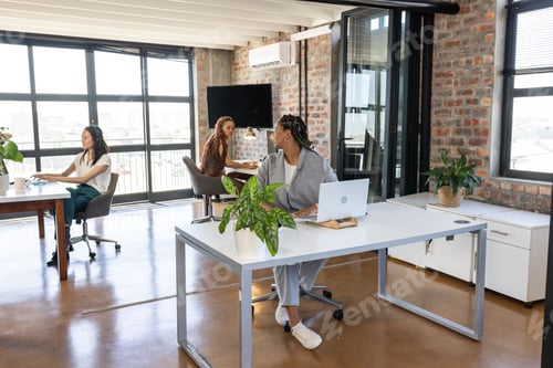 Preview: Colleagues in modern office collaborating and discussing ideas with laptops