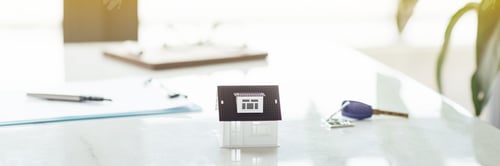 Preview: Working desk with tiny house on white marble background and blurred bokeh with copy space. Concept