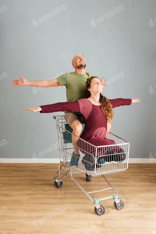 Preview: Man and Woman Sitting in a Shopping Cart With Their Arms Extended