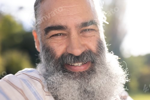 Preview: Caucasian senior man with grey beard, wearing light striped shirt, smiling outdoors