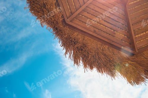 Preview: Beach umbrellas parasol made of coconut leaf standing on seashore against the backdrop of sunny blue