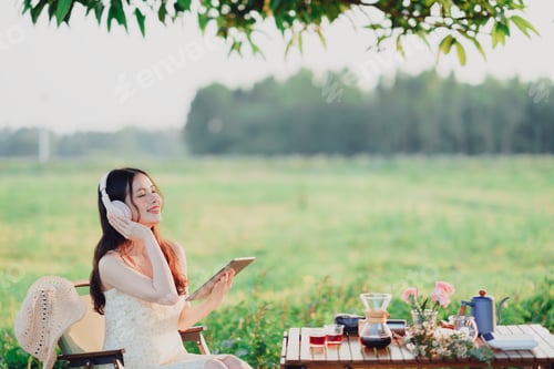 Preview: Woman with Headphones Relaxing Outdoors on a Green Field