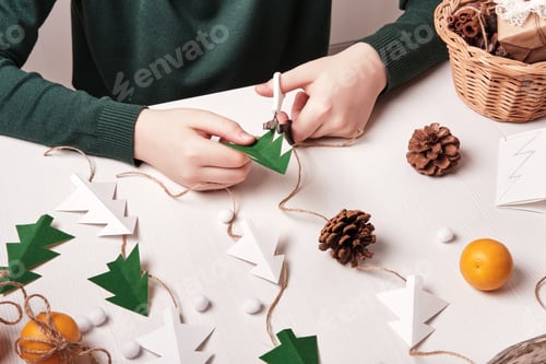Preview: DIY Christmas home decor from natural materials. Hands make garland of paper trees, twine and cones